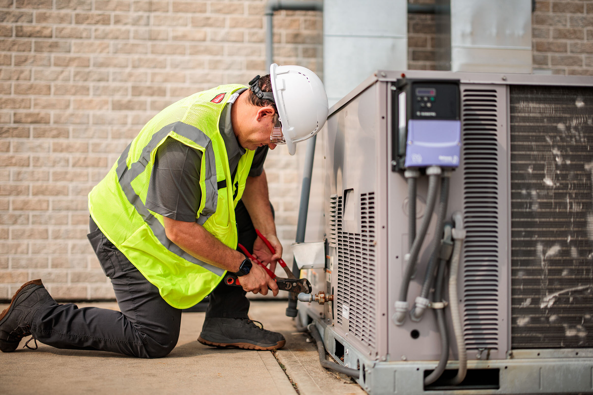 A GEM technician performs commercial HVAC maintenance on an outdoor HVAC unit.