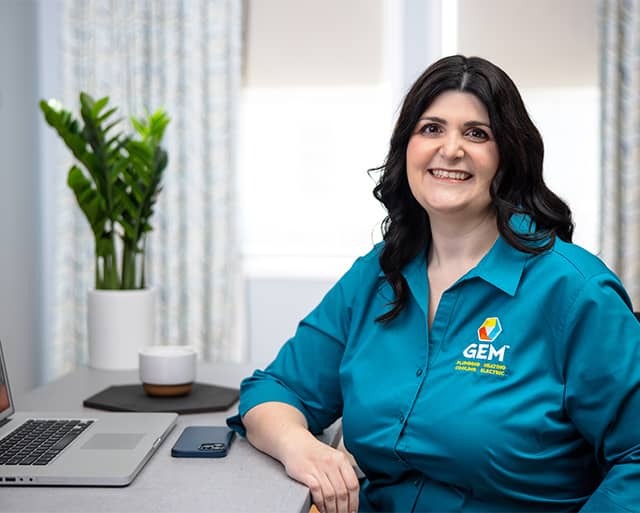 Female Gem Plumbing u0026 Heating employee sitting at a desk smiling