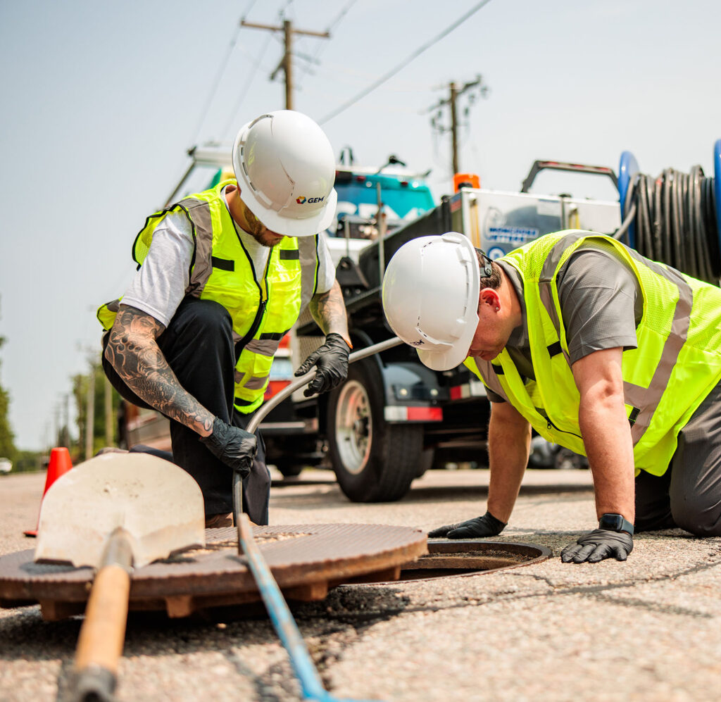Image of two GEM technicians inspecting sewer and pipe system for drainage or other plumbing issues.