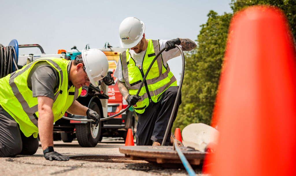 Image of two GEM technicians inspecting sewer and pipe system for drainage or other plumbing issues.