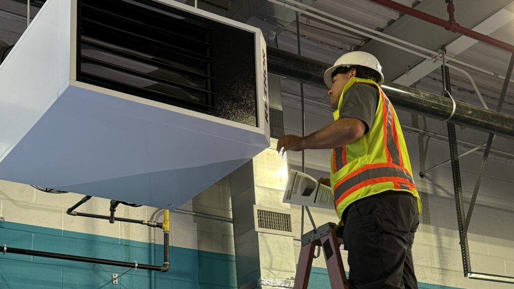 A tech fixes an HVAC system from a ladder. GEM can help you decide whether to repair vs replace a commercial HVAC system.