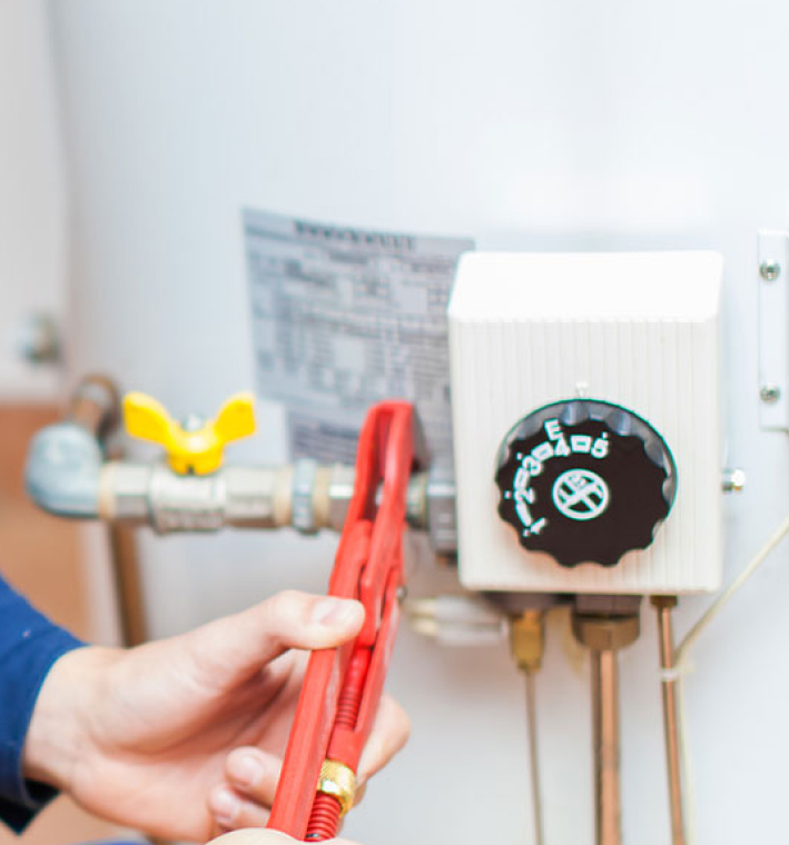Close up of a red wrench adjusting the pipe attached to a water heater.