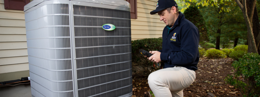 A GEM technician is performing spring hvac maintenance on an outdoor HVAC unit near a house, surrounded by greenery.