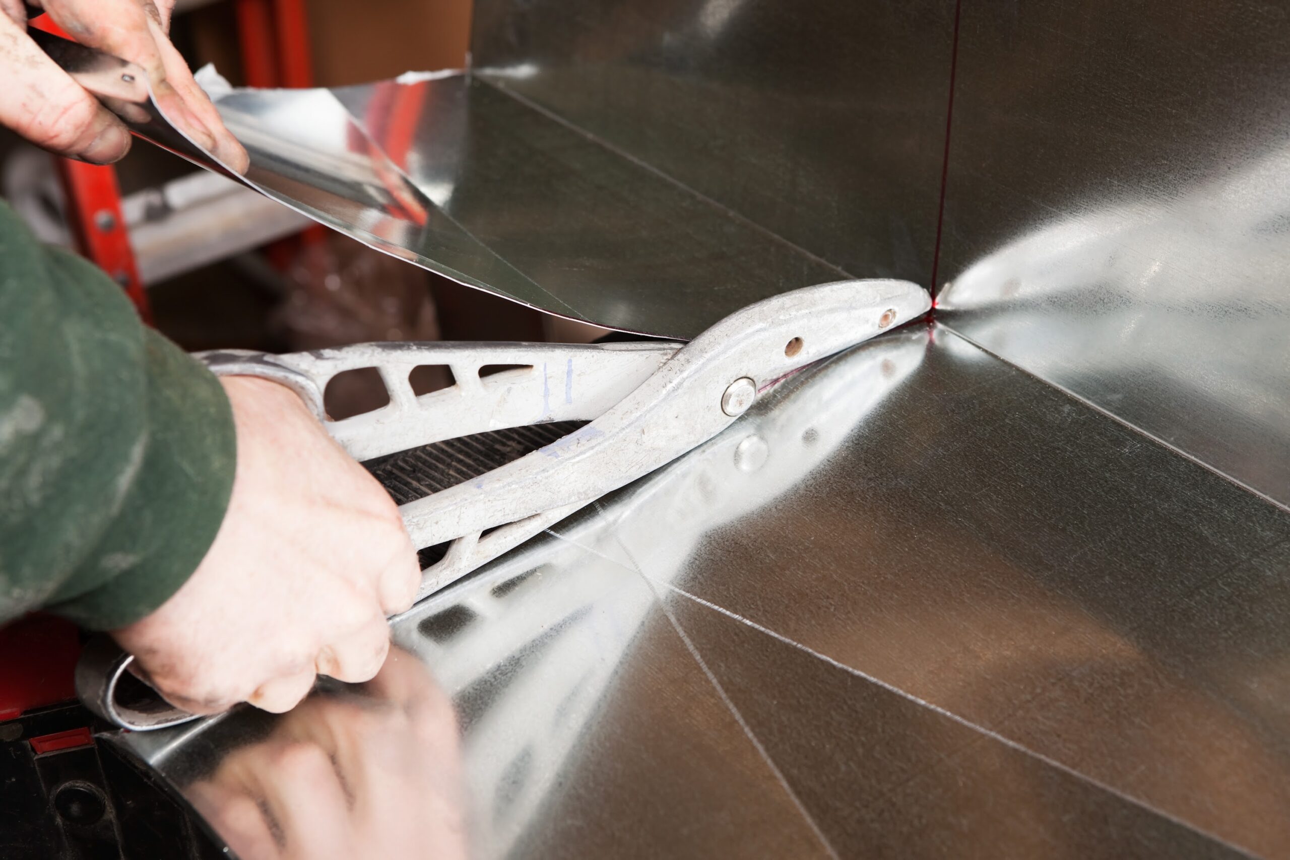 A HVAC installer is using large tin snips to trim a section of house air duct sheet metal. This is one of two angle pieces which will be assembled into a duct section.