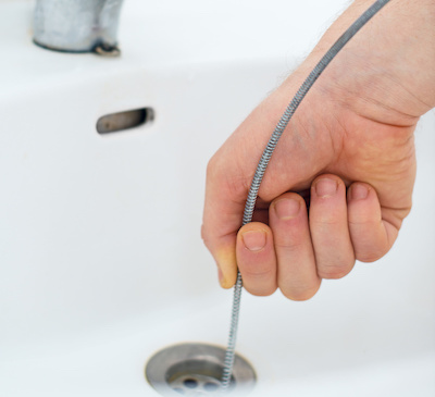 Plumber repairing sink with plumber's snake.