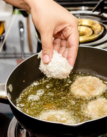 Person frying battered pork in oil on the stove