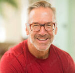 A man in a red shirt and brown glasses with white hair