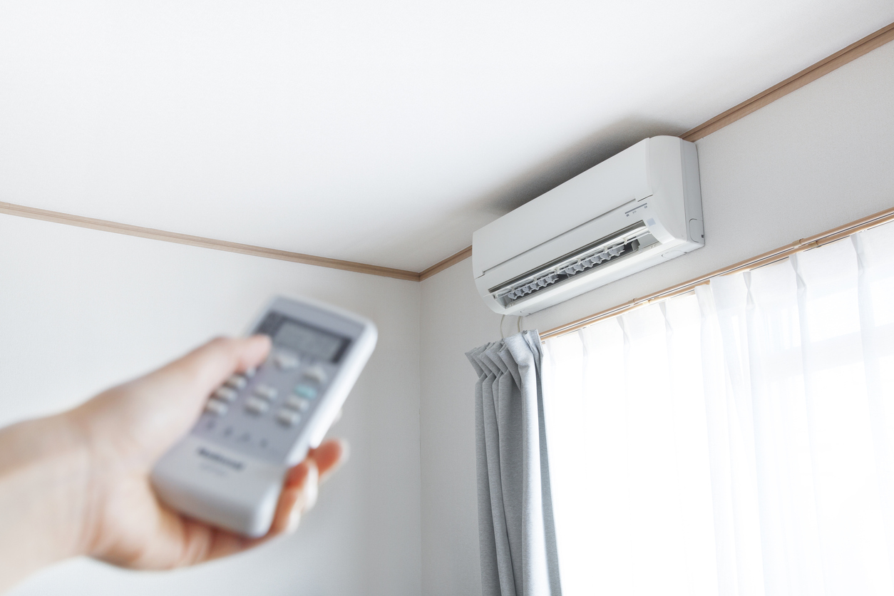 Hand with remote control pointing toward a ductless mini-split in a residential living room.