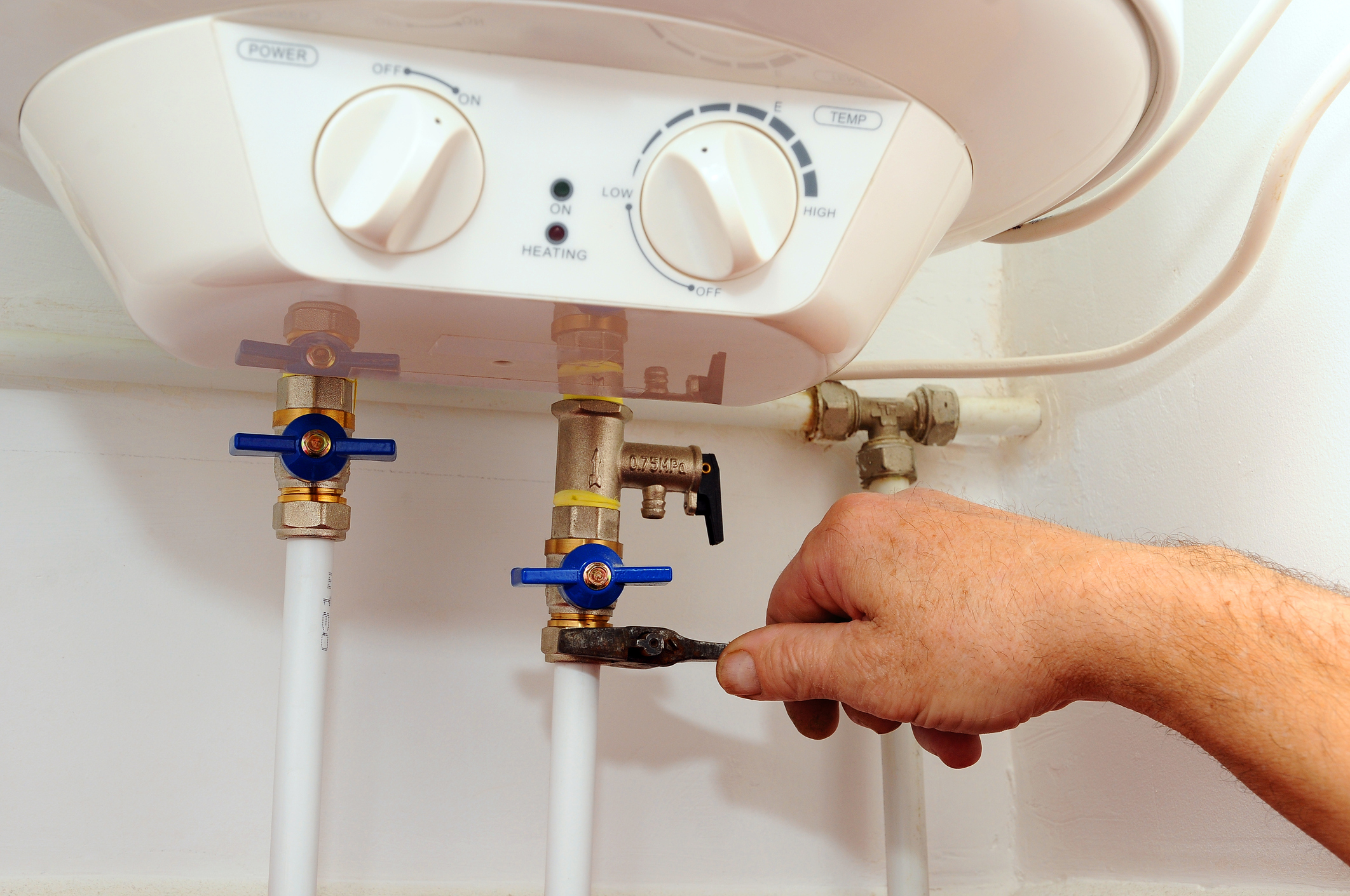 Male plumber's hand using a tool to tighten a connection on a tankless water heater.